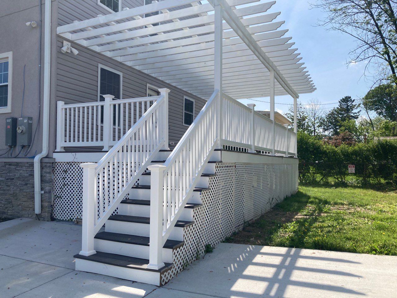 Outdoor staircase leading to a white wooden deck with lattice and pergola, adjacent to a house.